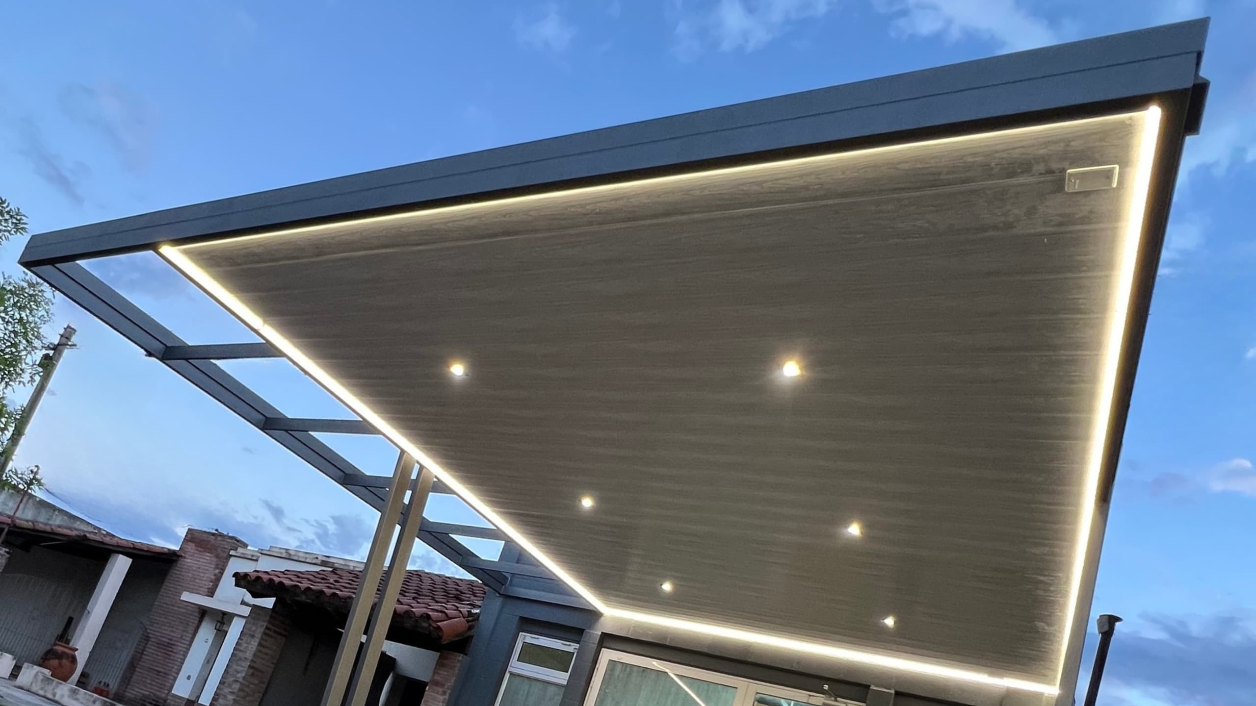 Pergola de aluminio con techo de vidrio y luces LED integradas en residencia moderna de noche
